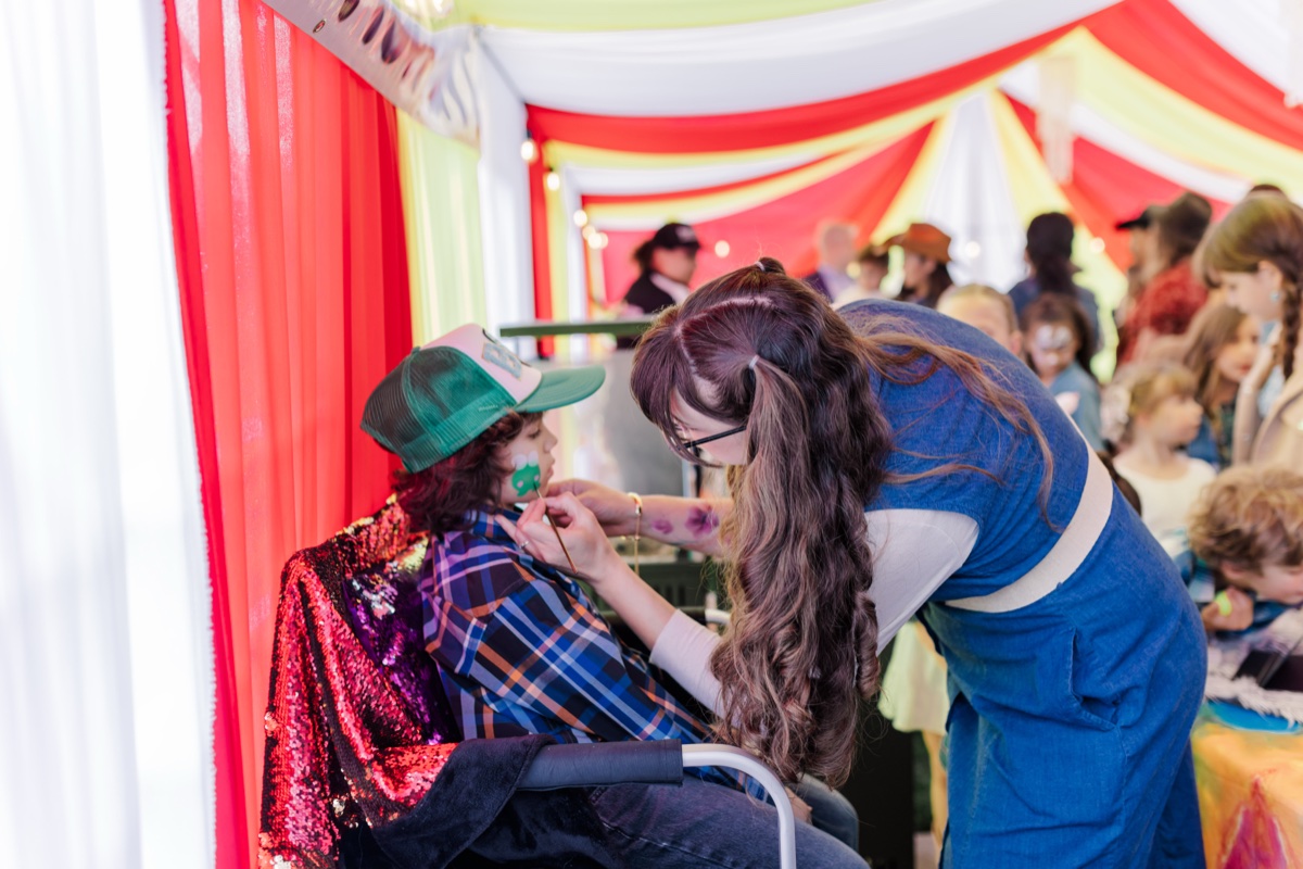 Candace painting a child's face at a colorful festival event